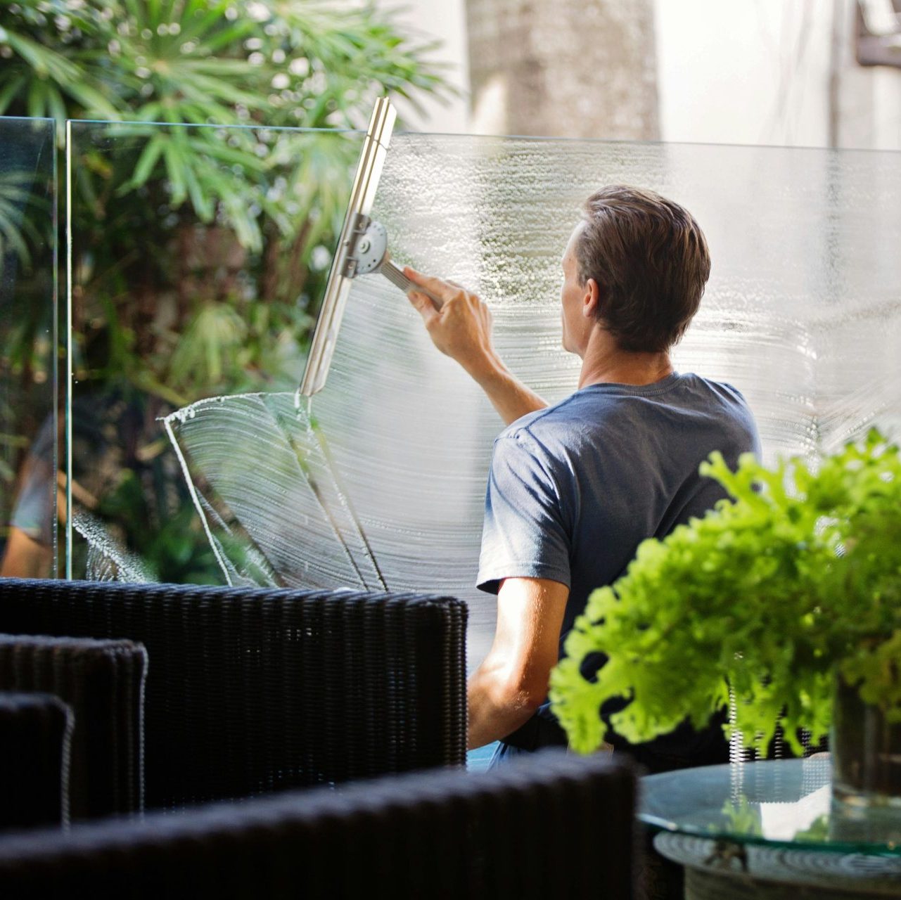 Man in Gray Shirt Cleaning Clear Glass Wall Near Sofa